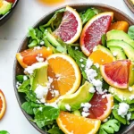 A fresh winter citrus and avocado salad with blood oranges, mandarins, avocado slices, arugula, and crumbled feta cheese in a rustic bowl.